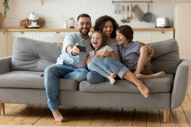 What Are the Signs that I Need a New Furnace? Photo of a family of four sitting on a couch together taking photos together.