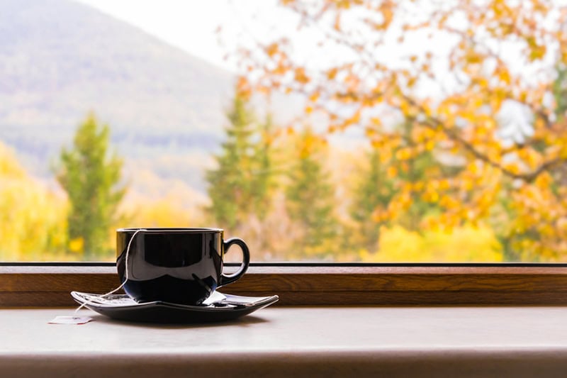 A black teacup and saucer sitting on a wooden windowsill.