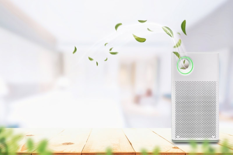 A modern white air purifier sitting on a light-colored wooden table or surface.